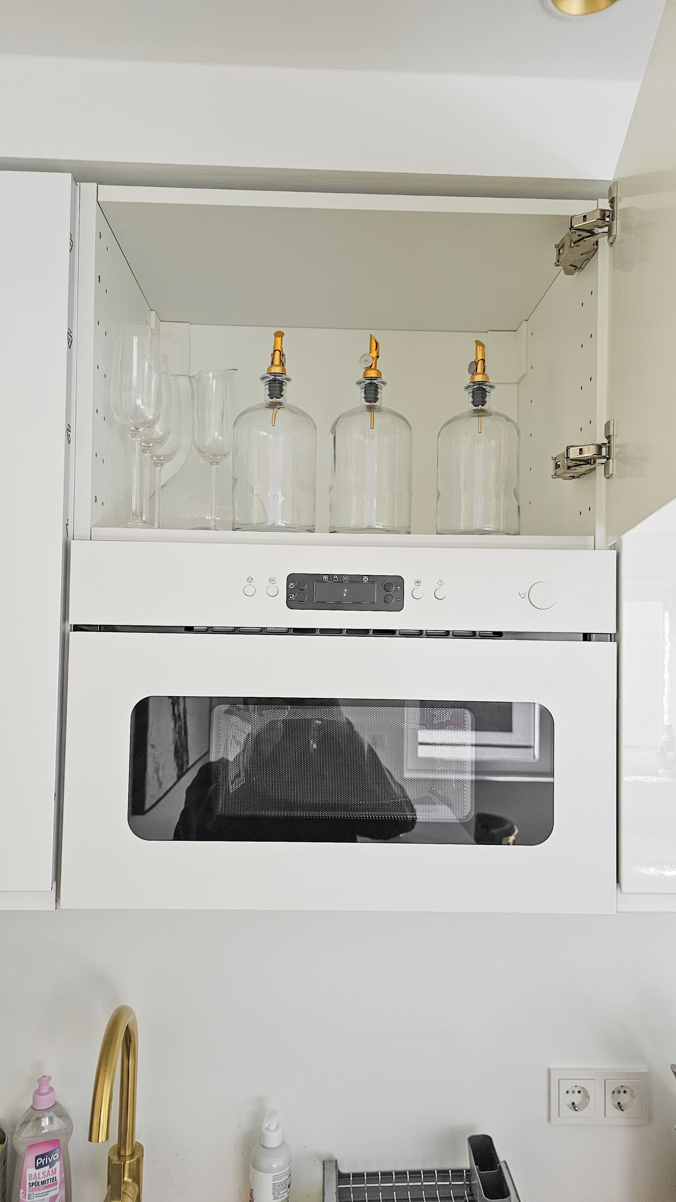Una cocina con estufa blanca, tres frascos de vidrio con tapas doradas y una puerta de horno negra.