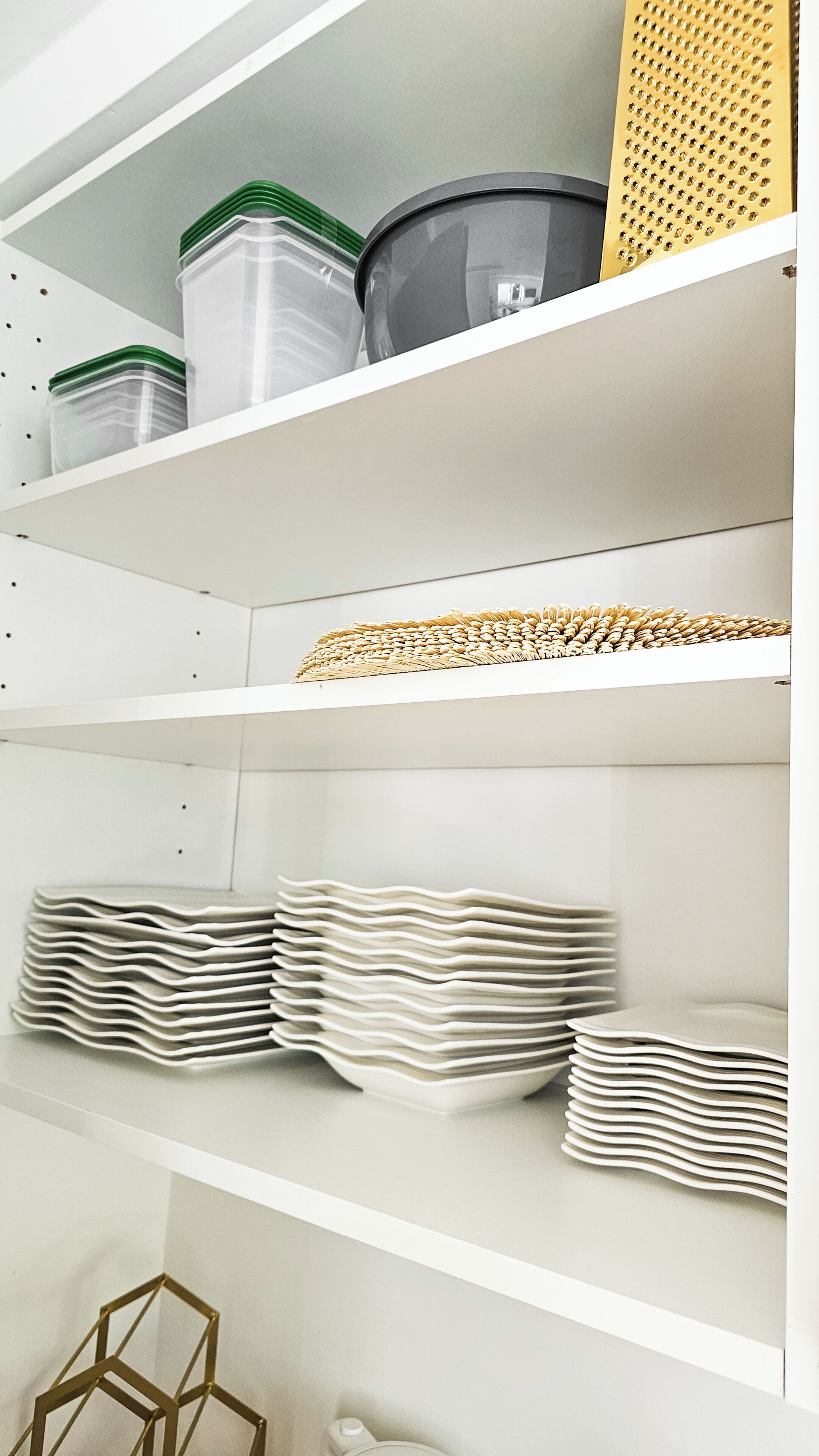 Un estante blanco con recipientes transparentes, una cesta tejida y platos apilados.