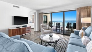 Een moderne hotelkamer met een ruim balkon, een flatscreen televisie, een bank, een stoel en een salontafel.