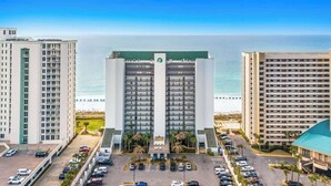 Een hoog hotel met meerdere verdiepingen, een parkeerplaats en uitzicht op de oceaan.