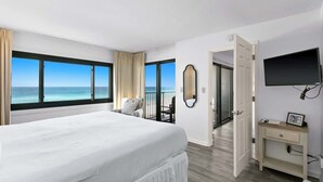 Een hotelkamer met een groot bed, een televisie, een bureau en uitzicht op de oceaan.