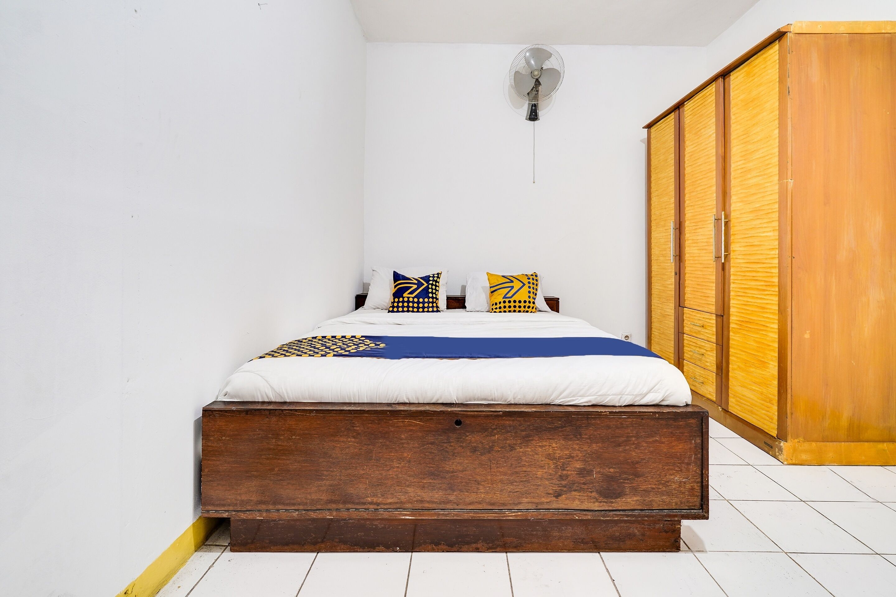 A bedroom with a wooden bed, white walls, a wooden wardrobe, and a ceiling fan.