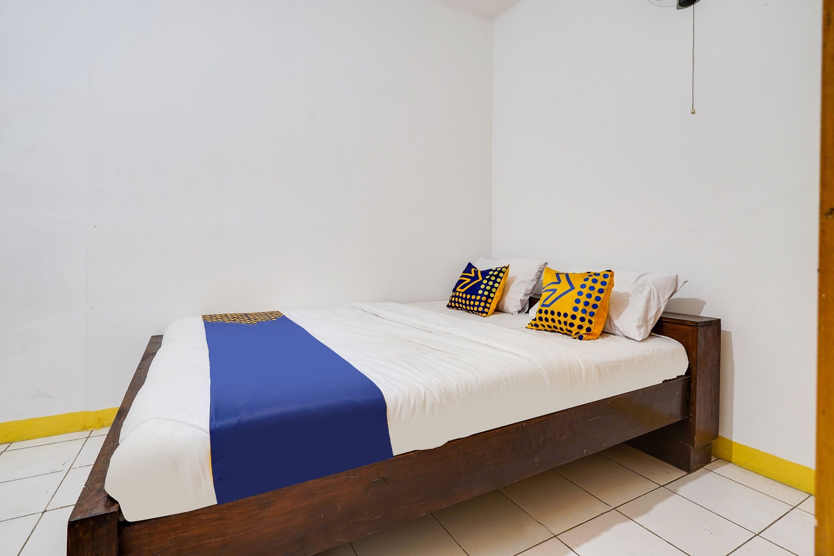 Un lit simple avec un cadre en bois, une literie blanche et des oreillers à motifs bleus et jaunes.