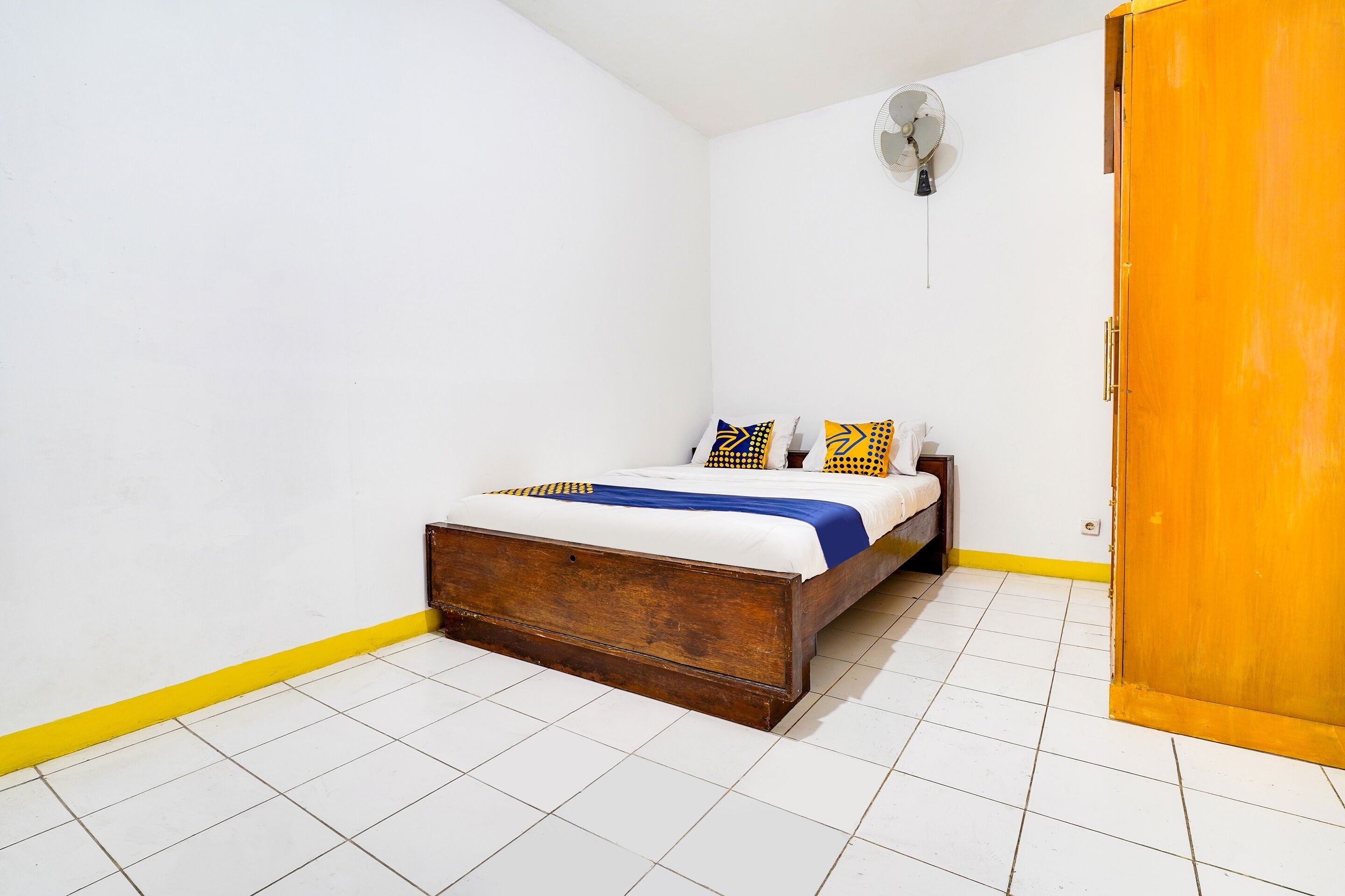 Une chambre avec un lit en bois, un sol carrelé de carreaux blancs, une bordure jaune et une porte en bois.