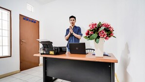 A person standing behind a desk with a laptop, a printer, and a vase of flowers. - OYO 91546 Dewi Sudirman Homestay (Bandung)