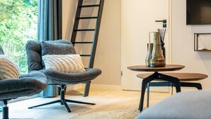 A modern living room with a grey armchair, a small round table, and a TV mounted on the wall. - Child-friendly house with trampoline (Voorthuizen)
