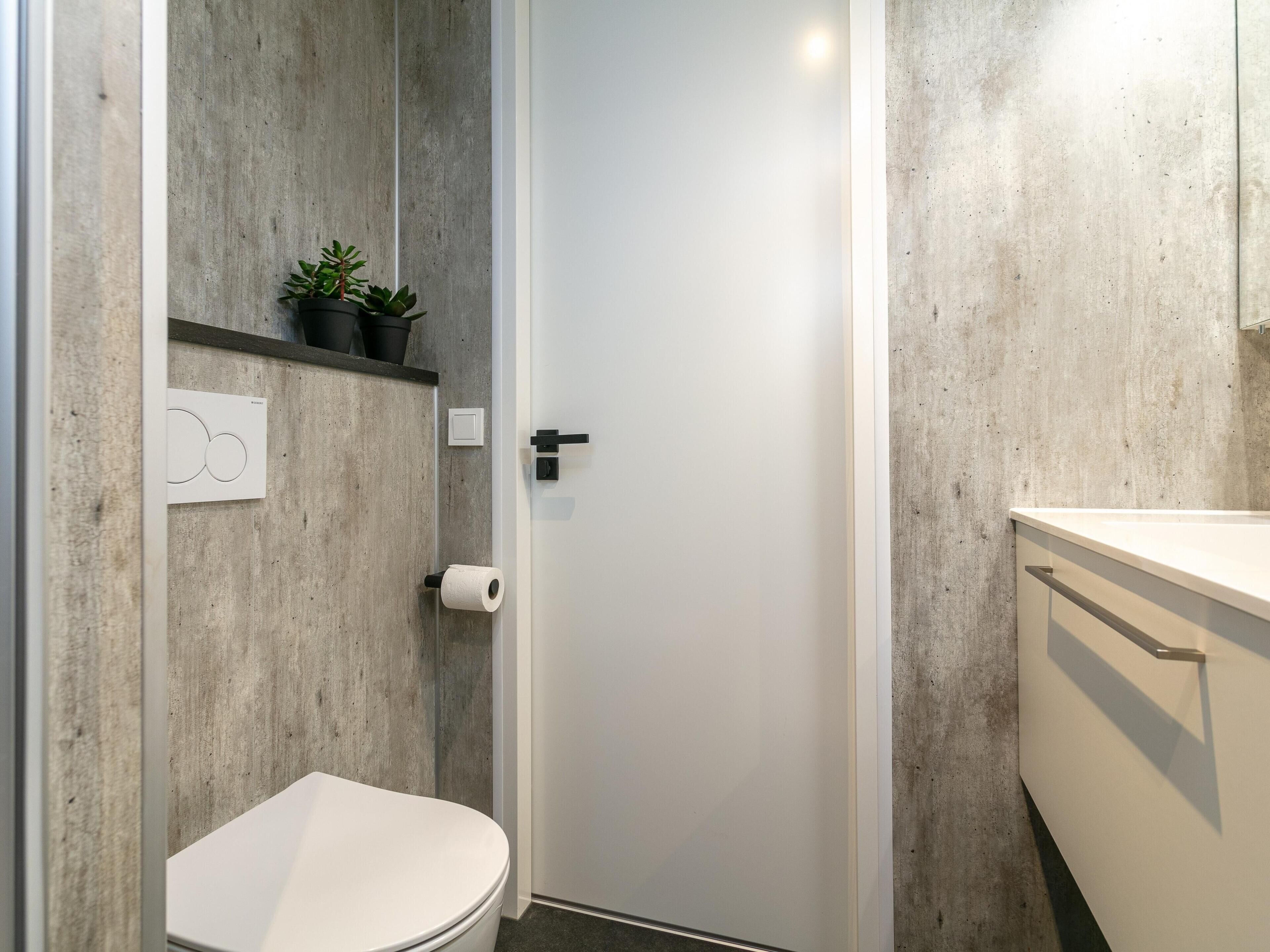 A modern bathroom with a concrete wall, a toilet, a sink, and a door with a handle.