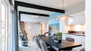 A modern dining area with a large table, grey upholstered chairs, and a hanging light fixture. - Child-friendly house with trampoline (Voorthuizen)