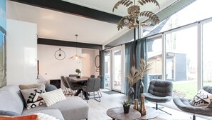 A modern living room with a large window, a dining area, and a seating area with a sofa and chairs. - Child-friendly house with trampoline (Voorthuizen)