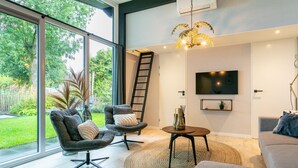 A modern living room with large windows, a flat-screen TV, and a ceiling fan. - Child-friendly house with trampoline (Voorthuizen)