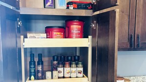 Un armario de cocina con estantes que contienen distintos utensilios, como botellas de aceite, condimentos y variedad de infusiones.