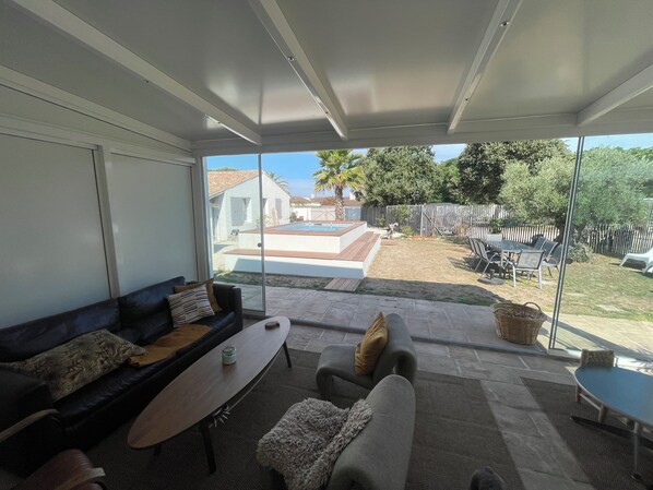 A modern living room with a large sliding glass door leading to a backyard with a pool and outdoor furniture.