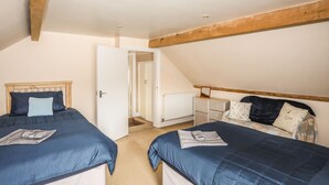 A bedroom with two beds, wooden beams, a white radiator, and a door leading to a staircase. - Garth (Pwllheli)