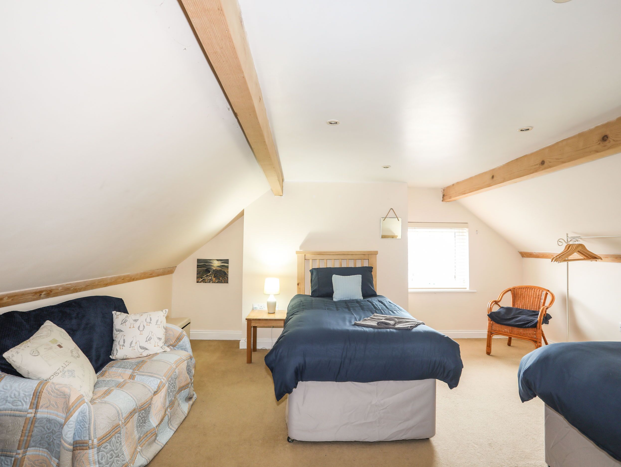 A cozy attic bedroom with a loft bed, a small bedside table, a chair, and a window.