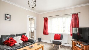 A living room with a black leather sofa, a wooden coffee table, a television, and a red curtain. - Garth (Pwllheli)