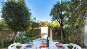 Un espacio de comedor al aire libre con una mesa dispuesta para dos personas, rodeado de follaje y un cielo despejado.