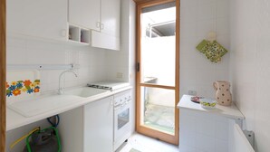 Una cocina pequeña con armarios blancos, un lavamanos, un horno y una ventana que da a un balcón.
