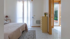 Un dormitorio con cama, cómoda, mesita de noche, lámpara, alfombra estampada y vistas al exterior.