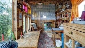 Ein rustikales Blockhaus-Interieur mit einem Holztisch, Stühlen, einem gemusterten Vorhang und verschiedenen Dekoartikeln.
