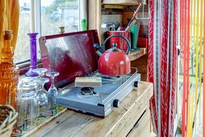 A rustic kitchen with a portable gas stove, a red kettle, and various kitchen utensils.