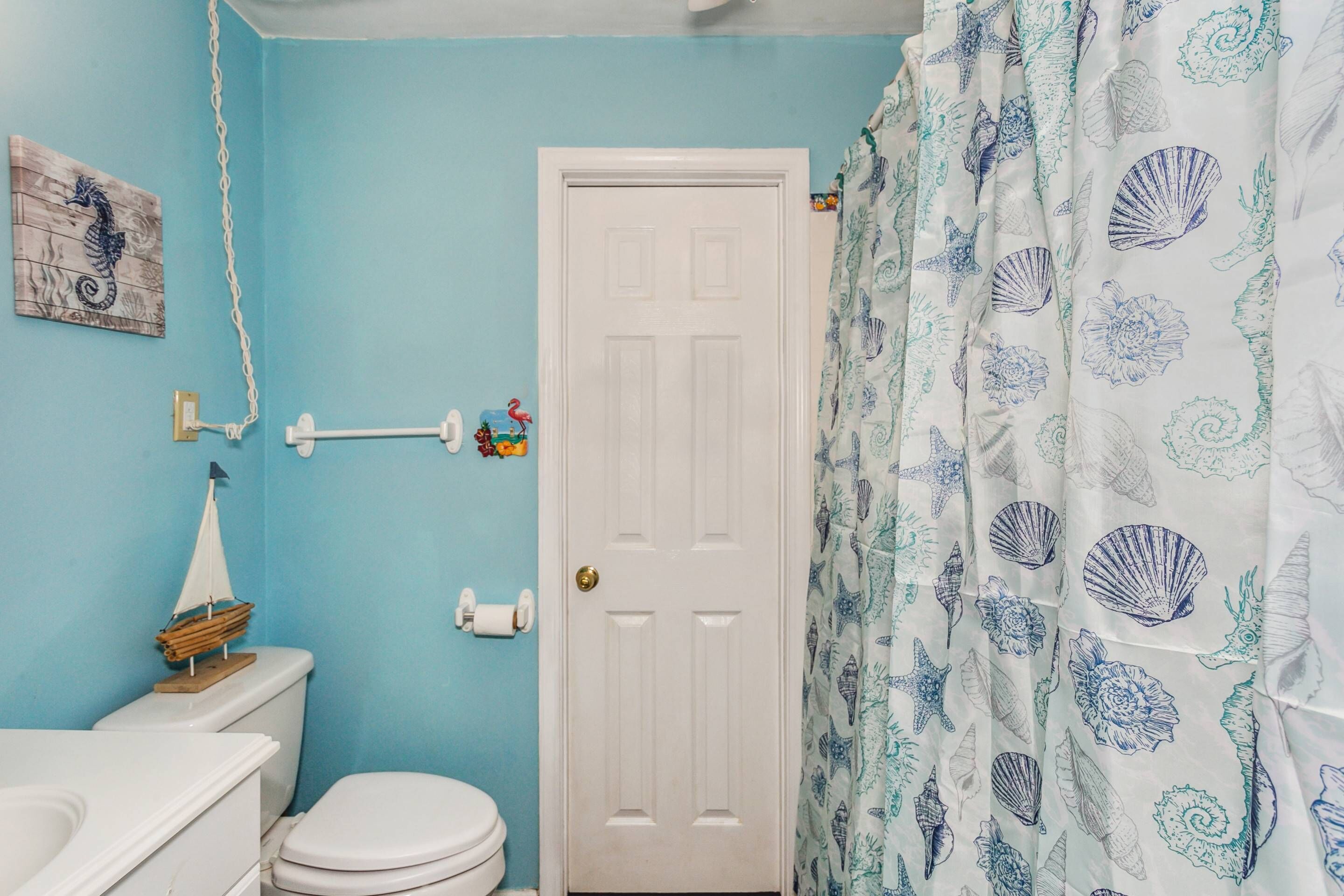 Een badkamer met een toilet, een wastafel, een witte deur en een douchegordijn met een zeeschelpenpatroon.