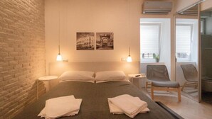 Una habitación de hotel moderna con una pared de ladrillo decorativa, una cama grande con toallas ordenadas, dos lámparas fijadas a la pared y una pequeña mesa redonda.
