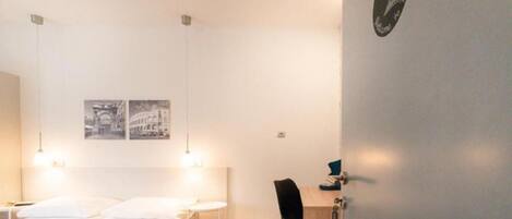 Una habitación de hotel moderna con cama, mesitas de noche, escritorio y silla. Hay dos luces empotradas en la pared sobre la cama y una lámpara en el escritorio.