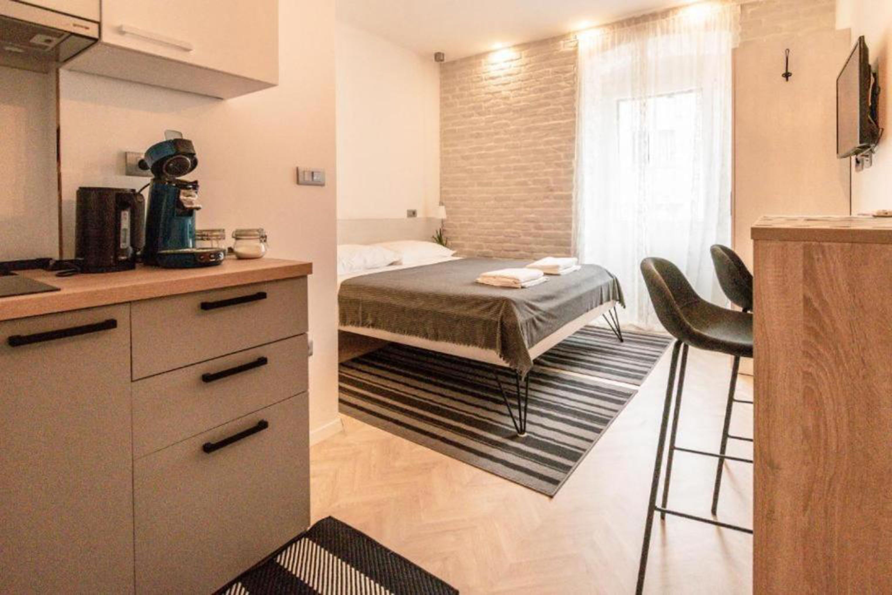 A modern hotel room with a bed, a desk with a coffee maker, a chair, and a TV.