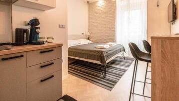 A modern hotel room with a bed, a desk with a coffee maker, a chair, and a TV.