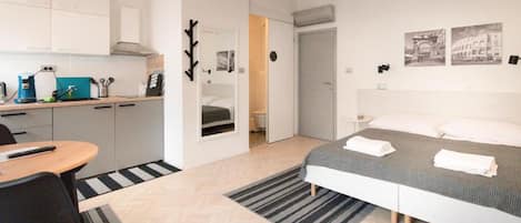 Een kleine hotelkamer met een bed, bureau, stoel, kitchenette en een badkamer.
