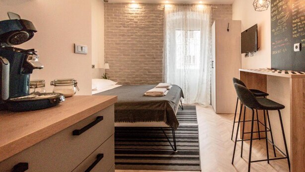 Una habitación de hotel compacta con cama, escritorio con silla, cafetera y televisión en la pared.