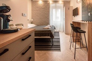 Una habitación de hotel compacta con cama, escritorio con silla, cafetera y televisión en la pared.