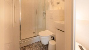 Un baño pequeño y moderno con cabina de ducha de vidrio, inodoro blanco y lavabo.