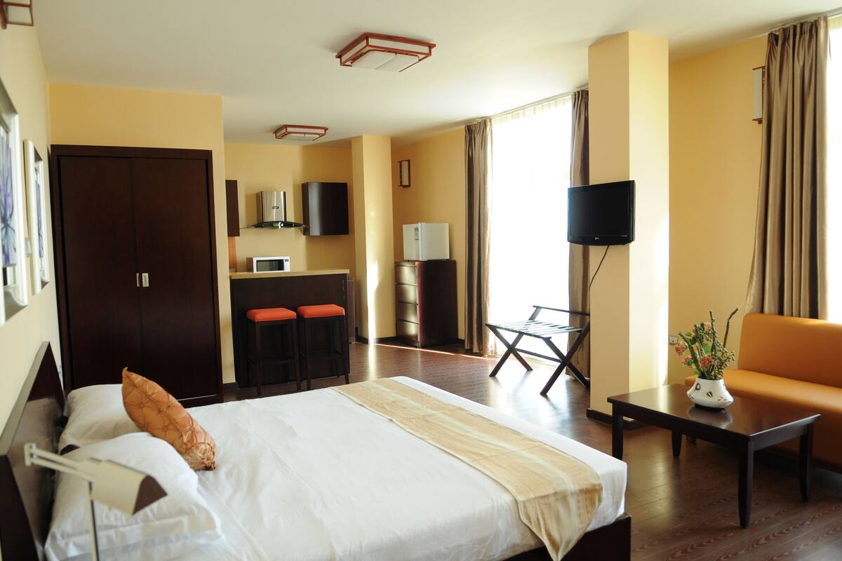 A hotel room with a bed, a desk, a chair, a TV, a microwave, and a refrigerator.