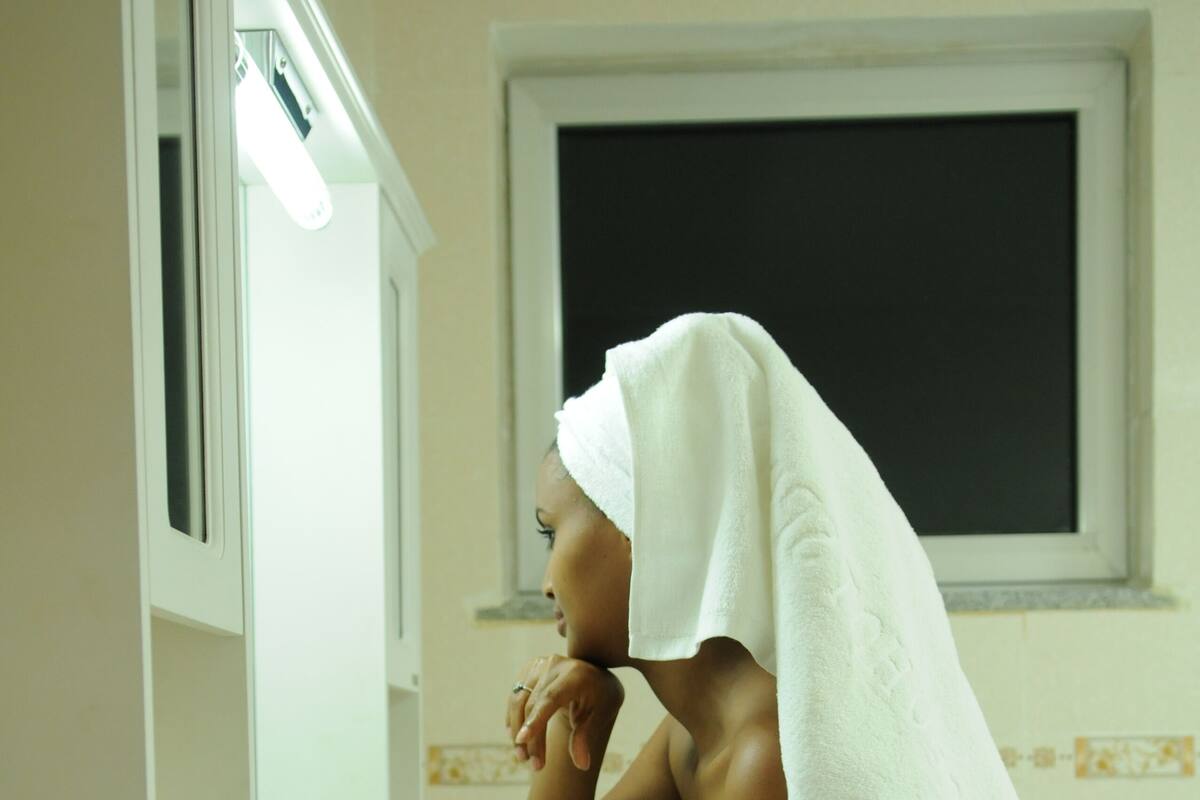 A bathroom with a white sink, a mirror, and a window above the mirror.