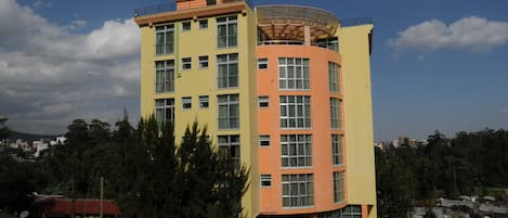 Un hotel de varios pisos con fachada amarilla y naranja, ventanas amplias y un letrero que indica que es un hotel.