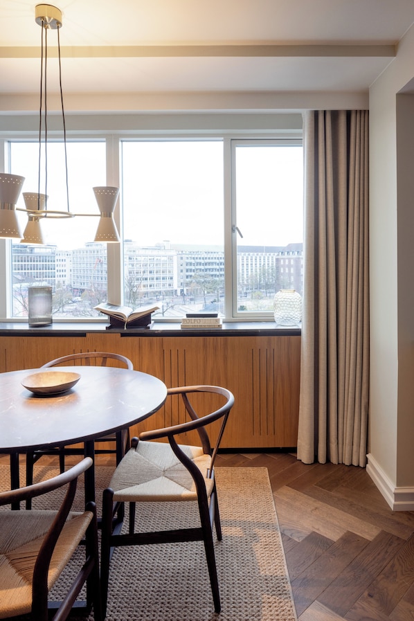 A dining area with a round table, chairs, and a view of the city through large windows.