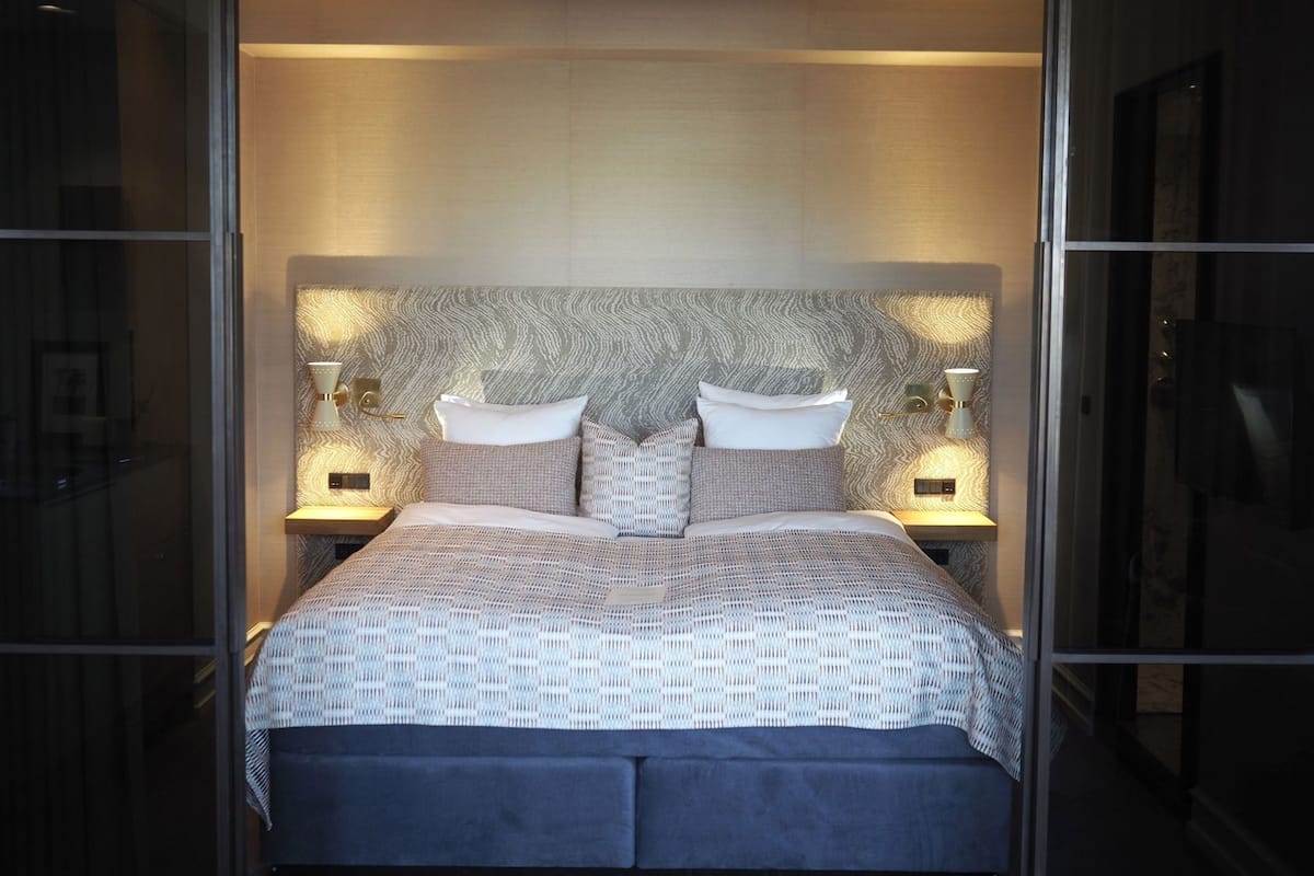 Un dormitorio moderno con un cabecero estampado, dos mesitas de noche con lámparas y una cama grande con colcha estampada.