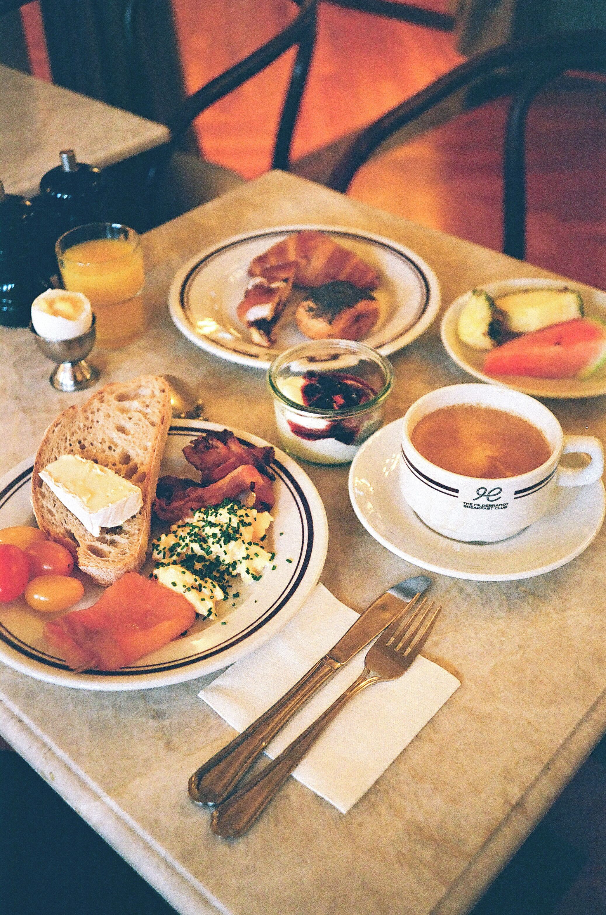 Una mesa de desayuno con platos de comida, una taza de café y un vaso de jugo de naranja.