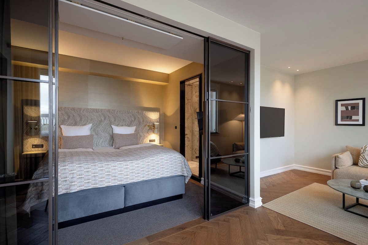Ein modernes Schlafzimmer mit einem großen Bett, einer Glastrennwand, einem Schreibtisch und einem Stuhl.