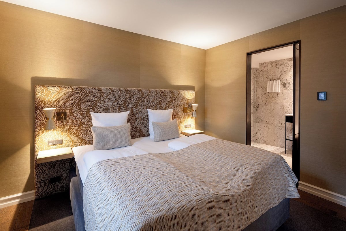 Ein Hotelzimmer mit einem großen Bett, zwei Nachttischen, einem Spiegel und einem Duschbereich.