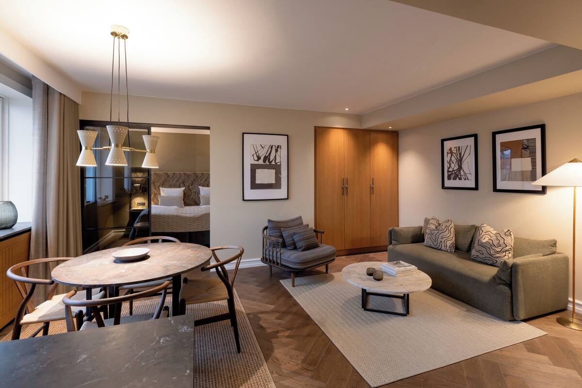 Una sala de estar moderna con sofá, mesa de centro y comedor. Hay cuadros enmarcados en las paredes y un mueble de madera.