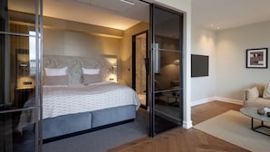 A modern bedroom with a large bed, a glass door leading to a balcony, and a small seating area with a table and chairs. - Hypernym Hotel & Suites (Copenhagen)