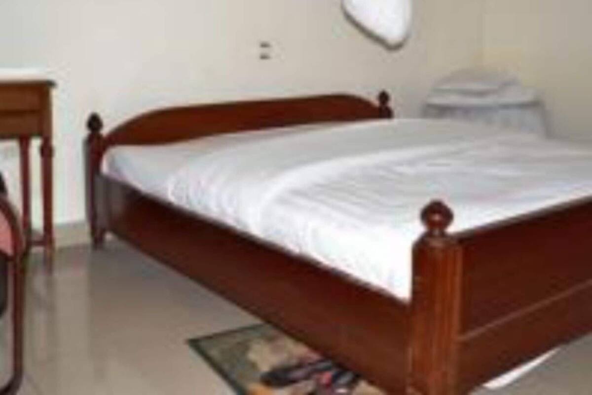 A single bed with a wooden frame, a bedside table, and a wall-mounted shelf.