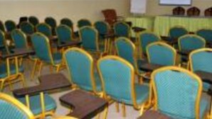 A conference room with rows of teal chairs and tables, a projector screen, and a chandelier.