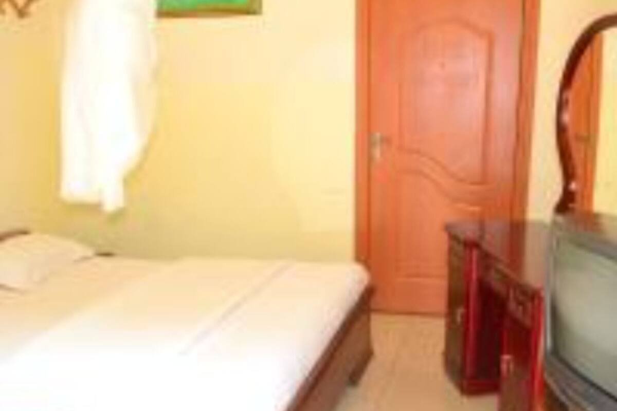A bedroom with a bed, a wooden dresser, a television, and a door.