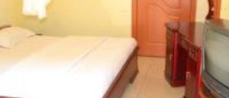 A bedroom with a bed, a wooden dresser, a television, and a door.
