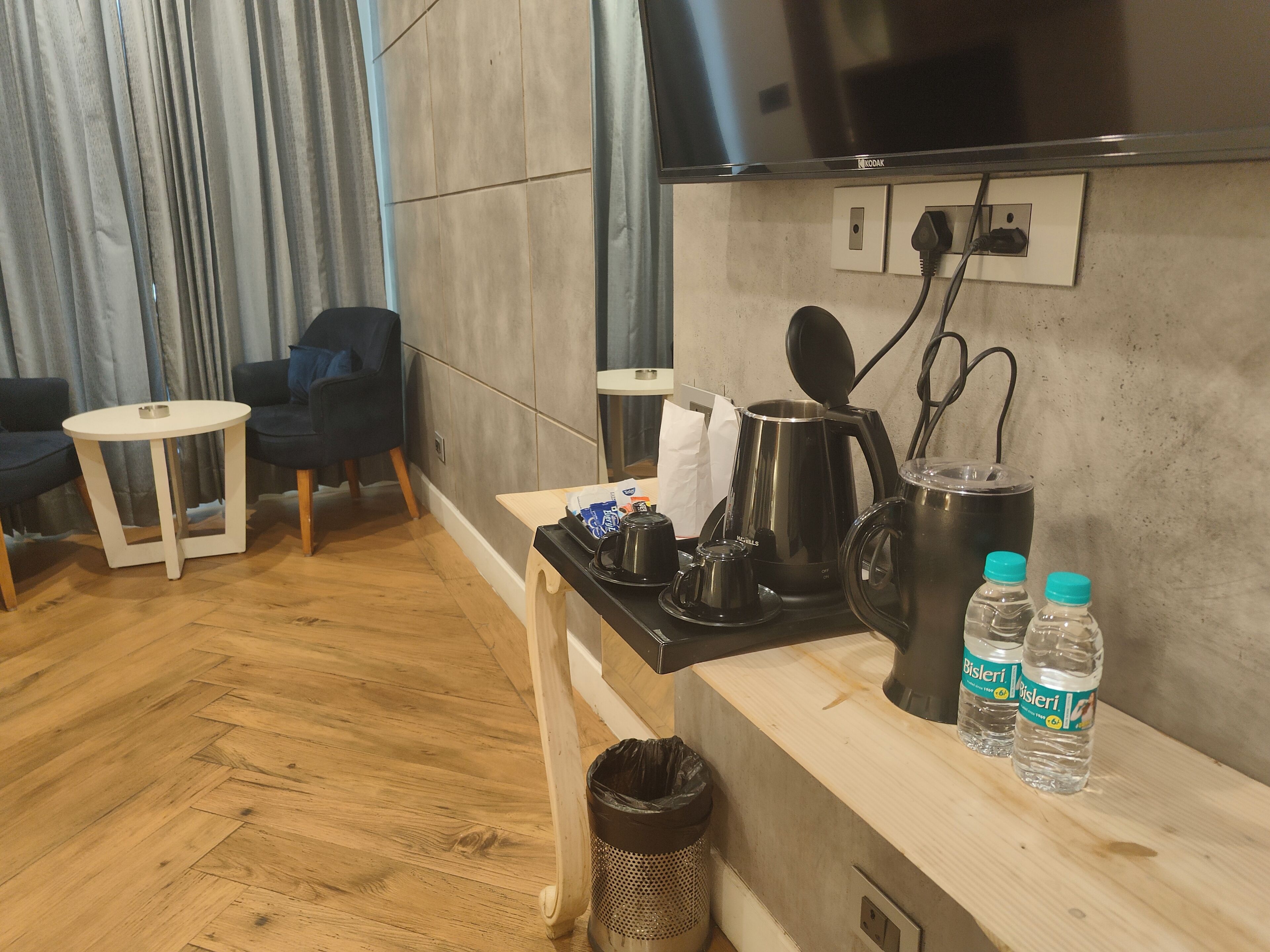 Zona giorno moderna con divano, un piccolo tavolino rotondo, angolo caffè con bollitore e televisore montato a parete.