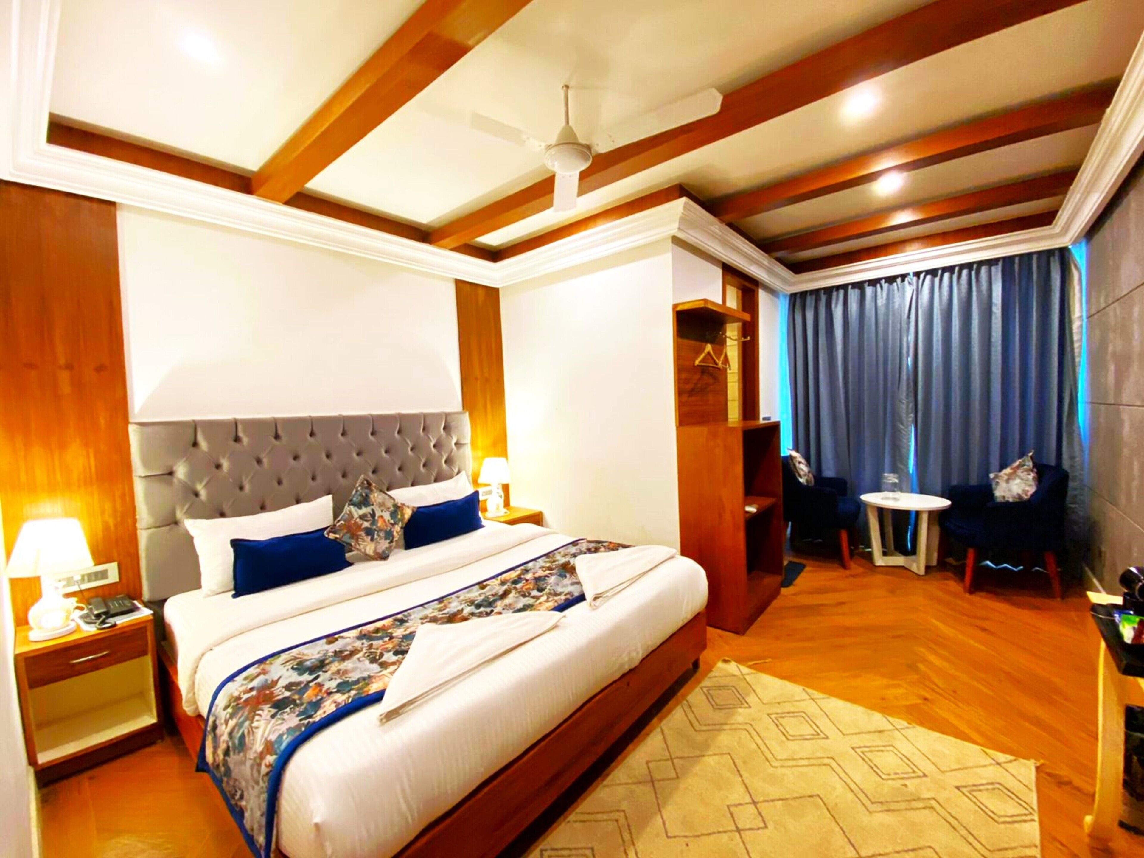A hotel room with a large bed, a ceiling fan, a small table, and a seating area with a view of the city.