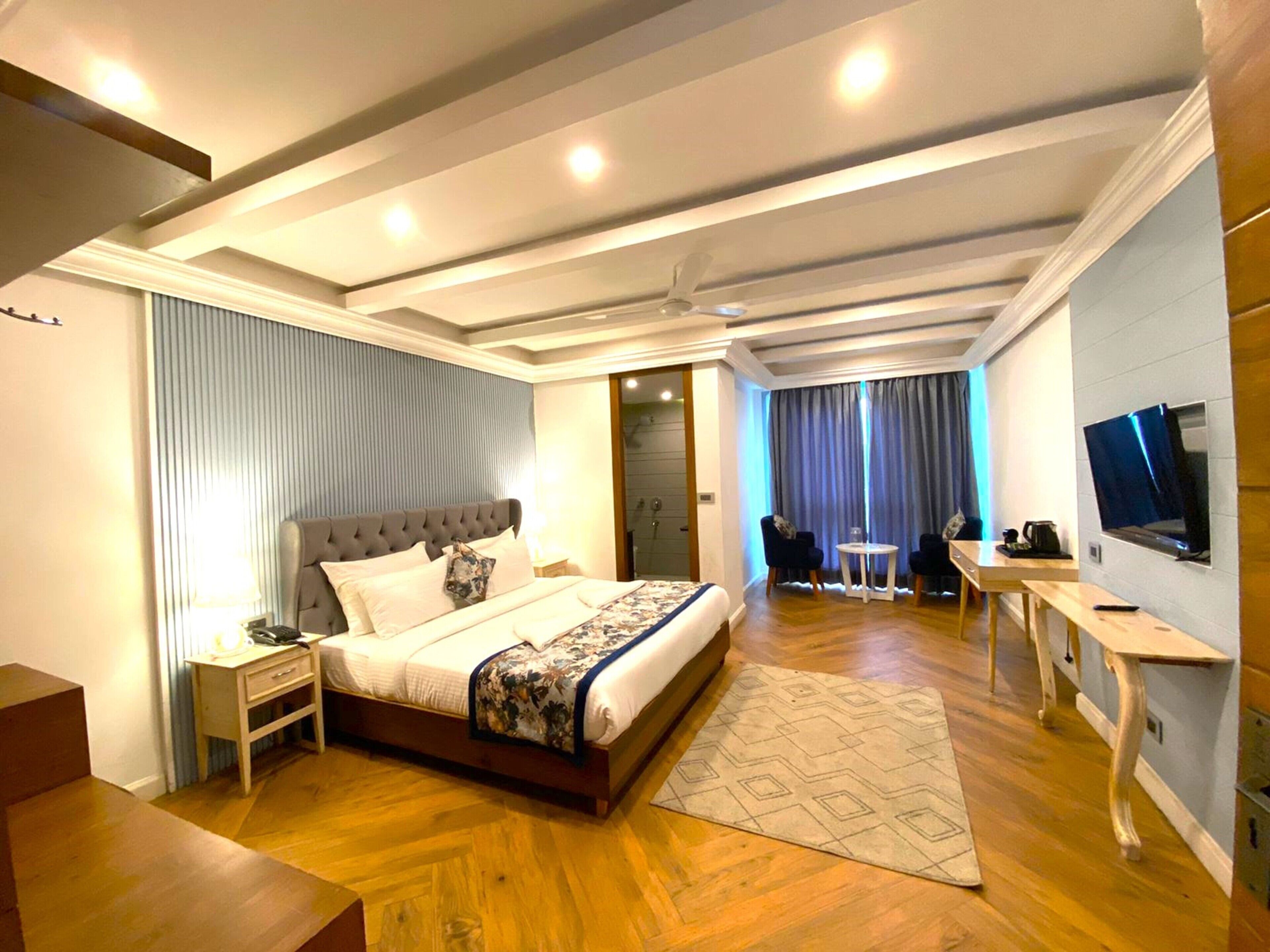 Une chambre d’hôtel moderne, dotée d’un grand lit, d’un bureau, d’une télévision et d’une salle de bain visible à travers une porte ouverte.